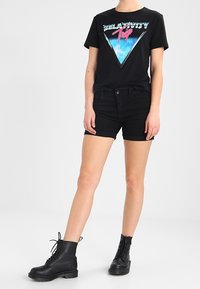 Černé grafické tričko s modrým a růžovým trojúhelníkovým designem. Doplňuje ho černé džíny šortky a černé šněrovací kotníkové boty.