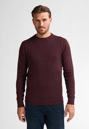Un pull en maille bordeaux à col rond avec des manches longues et des poignets côtelés, associé à un jean en denim bleu foncé.