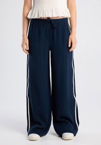 Navy wide-leg trousers with a lightweight fabric, elastic waistband, white side stripes, and a front tie detail.