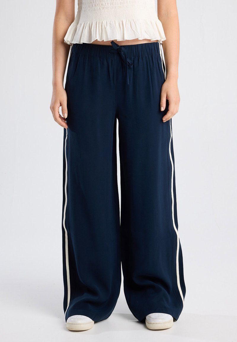 Navy wide-leg trousers with a lightweight fabric, elastic waistband, white side stripes, and a front tie detail.