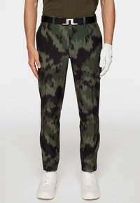 Kamouflage-mönstrade byxor i grön och svart; gjorda av ett glatt tyg; kombinerade med ett svart bälte med en silverspänne; vita skor.