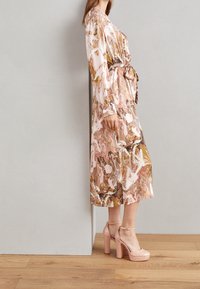 Abito a maniche lunghe, lungo fino alla caviglia, con un motivo marmorizzato rosa e oro, realizzato in tessuto morbido, abbinato a sandali con tacco alto rosa.