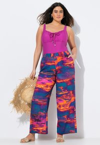 Felle roze tanktop met een verstelbare trekkoord, gecombineerd met wijde broekspijpen met oranje en blauwe abstracte patronen.
