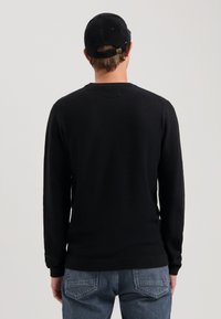 Schwarzer Strickpullover mit langen Ärmeln, gerippten Bündchen und strukturiertem Gewebe. Kombiniert mit hellblauen Jeans. Rückansicht gezeigt.