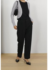 Vaaleanharmaa lyhyt neulejakku mustan t-paidan päällä, yhdistettynä korkeavyötäröisiin mustiin housuihin ja mustiin teräväkärkisiin korkokenkiin. Yksinkertainen, viimeistelty ilme.