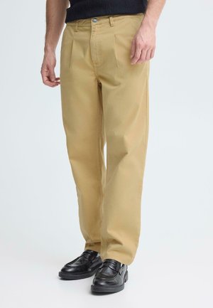 Chinos en coton beige à coupe droite, avec un devant plat et des poches latérales, portés avec des mocassins en cuir noir.