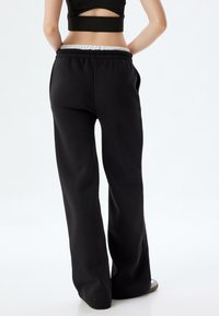 Zwarte sweatpants hebben een relaxte pasvorm, een elastische tailleband en twee zijzakken, met een gladde textuur en geen zichtbare patronen.