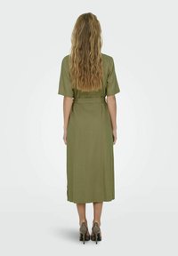 Olive roheline, keskmise pikkusega kleit pehmest kangast, millel on lühikesed varrukad ja seotud vöökoht. Tekstuur näeb välja sile, nähtavaid mustreid ei ole.