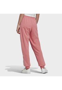 Růžové tepláky s elastickým pasem a manžetami, s postranními pruhy a uvolněným střihem. Nošeny s bílými teniskami.