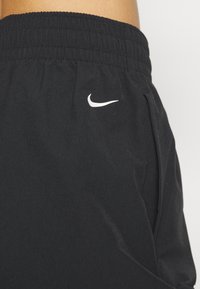 Black athletic shorts with an elastic waistband, side pockets, smooth texture, and a white Nike logo on the front.