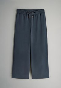 Pantaloni larghi grigio scuro realizzati in tessuto morbido, con una vita elasticizzata e un cordoncino, e dettagli metallici in tono oro.