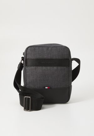 Grijze stoffen schoudertas met zwarte accenten, voorzien van een logo-harnas, ritssluiting en een klein rood, wit en blauw detail aan de onderkant.