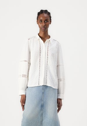 Weißes Hemd mit Knöpfen und strukturiertem Stoff, dekorativen Ösenmustern und langen Ärmeln, kombiniert mit einem hellblauen Denim-Rock.