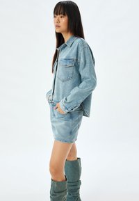 Ljusblå denimjacka med två framfickor, kombinerad med en matchande denimminikjol och knähöga denimstövlar. Slät textur.