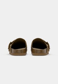 Pair of brown slip-on sandals with open backs and adjustable side straps, viewed from the heel on a white background.