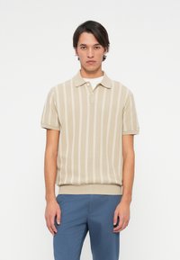 Beige triibuline polo särk, lühikesed varrukad, ribatud krae ja ääred. Kerge tekstuur koos valgete vertikaalsete triipudega. Koos siniste pükstega.