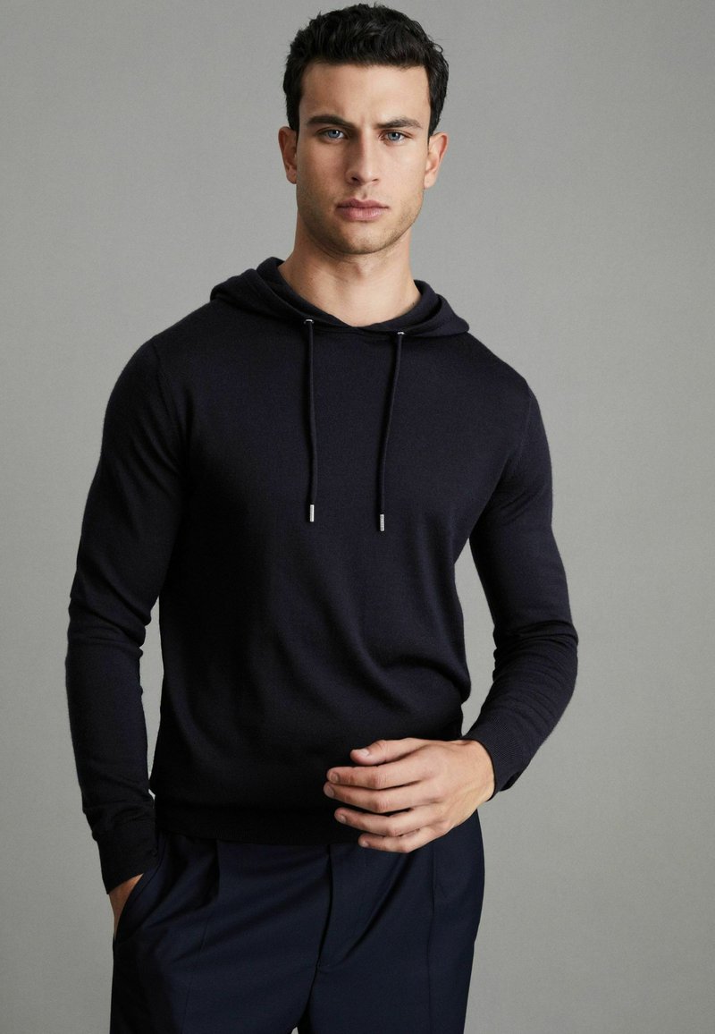 Sudadera oscura color navy con un corte relajado, mangas largas y cordones ajustables, que presenta una textura suave y un sutil brillo.