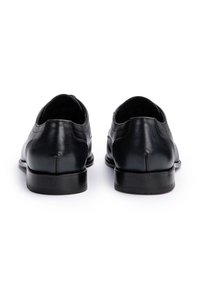 Een paar zwarte leren nette schoenen, gezien vanuit de achterkant met lage hakken, op een witte achtergrond.