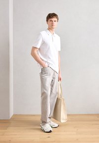 White polo shirt, light gray jeans, and white sneakers with green accents. Carrying a beige tote bag. Simple, casual design.