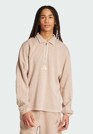 Beige pullover i blødt stof med en halv-zip krave, med ribbede manchetter og et lille broderet logo på brystet.