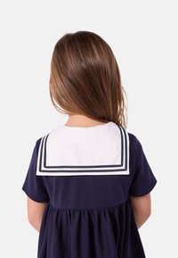 Μπλε φόρεμα ναυτικού στυλ με κοντά μανίκια, που διαθέτει λευκή γιακαδιά ναυτικού με μπλε ρίγες και ζώνη στη μέση που δίνει όγκο. Εμφανίζεται η πίσω όψη.