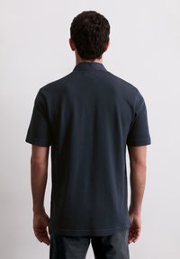 Granatowa koszulka polo z krótkim rękawem, z płaskim kołnierzykiem, miękką teksturą i prostym wykończeniem. Minimalistyczny design bez widocznych wzorów czy akcentów.