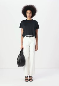 Camiseta negra corta, pantalones anchos blancos, cinturón negro y bolso negro. La modelo lleva sandalias negras con detalles en plata.