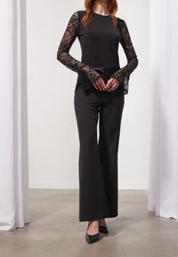 Svart långärmad topp med spettdetaljer och figurnära kropp, i kombination med högmidjade svarta vida byxor och spetsiga svarta klackar.