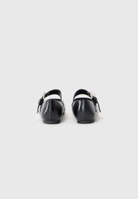 Schwarze Lederballerinas mit runder Spitze und einem Riemen hinten, verziert mit einer silbernen Schnallenakzentuierung. Glatte Textur und minimales Design.