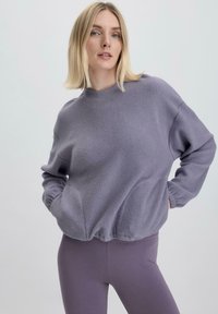 Lila Fleece-Pullover mit rundem Halsausschnitt, überschnittenen Schultern und elastischen Bündchen, kombiniert mit passenden Leggings für einen abgestimmten Look.