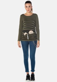 Langarm-Oliv-T-Shirt mit schwarzen horizontalen Streifen, featuring ein Cartoon-Baby-Graphic und einem silbernen Kettenakzent am Saum.