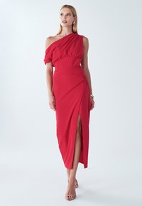 Red one-shoulder dress with gathered bodice, side slit, and smooth texture. Features a fitted waist and floor-length design.