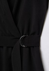 Vêtement en tissu noir avec une ceinture à la taille munie d'une boucle double anneau argentée.
