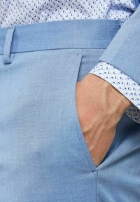 Ljusblå byxor med en slät yta, med en sidoficka. En mönstrad vit och blå skjortärm är synlig, som visar cirkulära mönster.