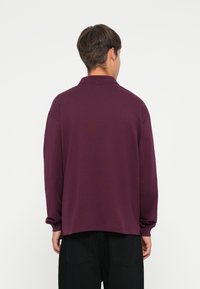 Purple long-sleeve polo shirt with a relaxed fit, folded collar, and dropped shoulders, made from a soft textured fabric.