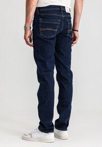 Ciemnoniebieskie dżinsy z prostym krojem, kontrastującymi przeszyciami oraz dwoma tylnymi kieszeniami ozdobionymi wzorem szczytu góry.