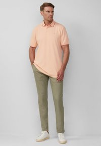 Helles Pfirsich-Polohemd mit Kragen und zwei Knöpfen, kombiniert mit olivgrünen Hosen. Weiße Sneaker runden das Outfit ab.