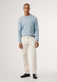 Maglione azzurro chiaro, jeans color crema, scarpe nere. Il maglione ha il collo rotondo e polsini aderenti; i jeans presentano una leggera texture.