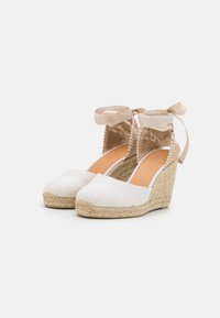 Espadrillas bianche con zeppa in tela e suola in giuta, dotate di un retro testurizzato e nastri color nocciola per una serratura sicura alla caviglia.