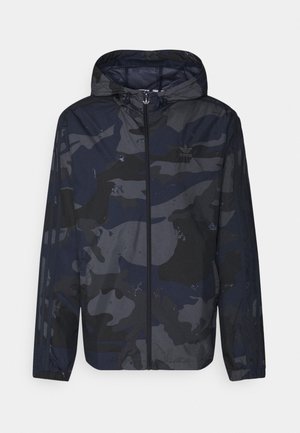 Herenhoodie met ritssluiting met donkerblauw en zwart camouflagepatroon en Adidas-logo op de borst, waterdruppels op het oppervlak.