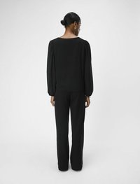 Zwarte blouse met pofmouwen en een ronde halslijn, gecombineerd met zwarte rechte broek, bekeken vanuit de achterkant.
