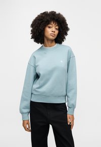 Ανοιχτό μπλε φούτερ από απαλό βαμβακερό μείγμα, με στρογγυλή λαιμόκοψη, ριμπ μανσέτες και διακριτικό λογότυπο στο στήθος.