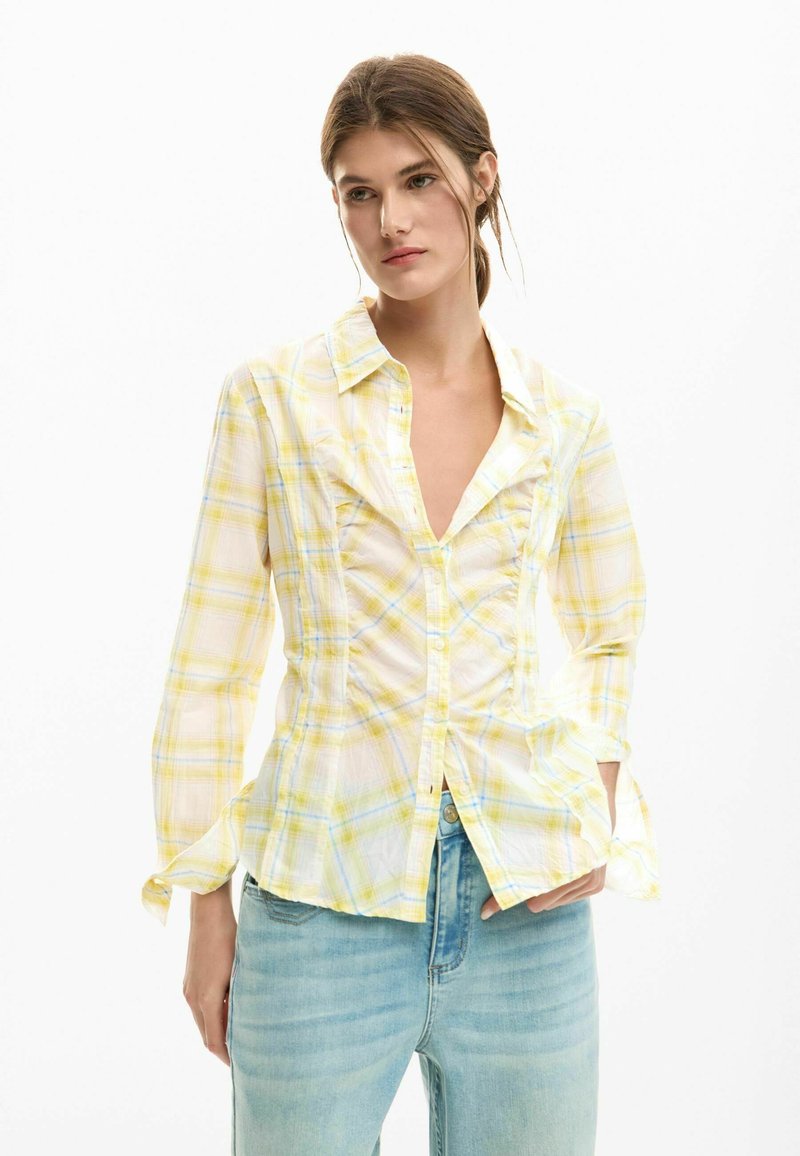 Chemise à carreaux jaune avec un devant à boutons, manches longues et tissu texturé. Présente des détails froncés le long du corsage et un col ouvert.