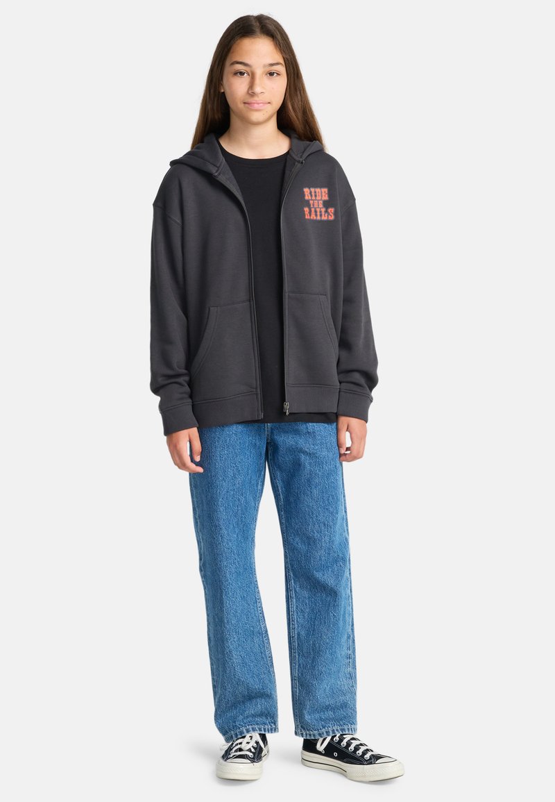 Grijze zip-up hoodie met oversized pasvorm, voorzakken, en "RIDE THE RAILS" in het rood gedrukt. Gecombineerd met blauwe rechte spijkerbroek en zwarte sneakers.