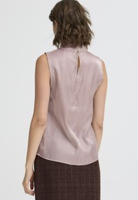Blusa senza maniche in satin rosa chiaro con un collo alto e un dettaglio a chiave sul retro. Texture liscia, design fluido e vestibilità rilassata.