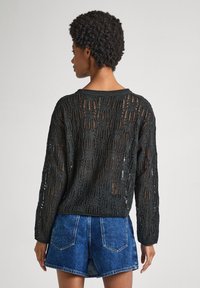 Svart stickad tröja med öppen, strukturerad mönster; långa ärmar och rundad halsringning. Matchad med denimshorts.