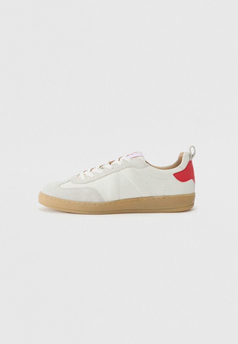 Fehér sneaker velúr és bőr anyagokból, gumi talppal, piros sarok akcentussal, rózsaszín logóval a nyelvén és klasszikus fűzős kialakítással.