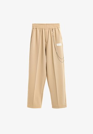 Pantalones beige de pierna ancha con cintura elástica, bolsillos laterales, pliegues delanteros y una cadena plateada decorativa unida cerca de una pequeña etiqueta blanca en el lado derecho.
