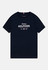Granatowa bawełniana koszulka z krótkim rękawem, z białym napisem "Tommy HILFIGER" oraz "Est. 1985" poniżej. Zawiera mały akcent w postaci logo.
