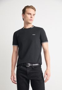 Sort kortærmet T-shirt med hvid stribet ribkant og "BOSS" logo. Bæres med mørke jeans og sort bælte. Glat stof, afslappet pasform.